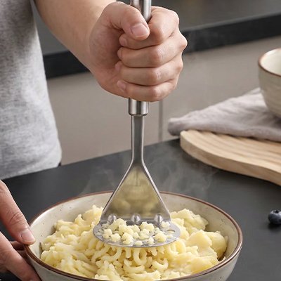 homme écrase pommes de terre dans bol céramique utilisant presse purée