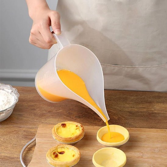 cuisinier verse crème anglaise du verre doseur dans tartelettes