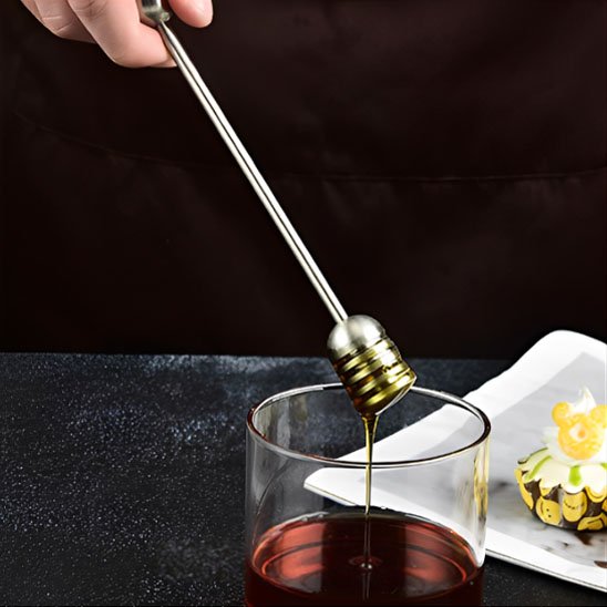 Cuillère à miel inox versant miel dans un verre