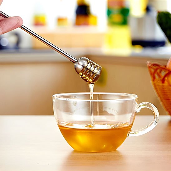 Cuillère à miel inox laissant couler miel dans tasse de thé