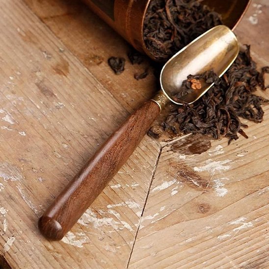 Cuillère à thé gongfu éffilée sur table bois avec feuilles thé autour