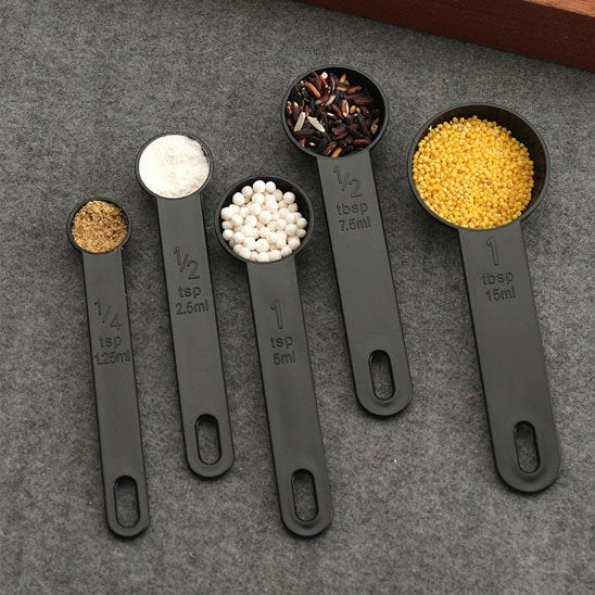 cinq uillères doseuses plastique noire remplies de graines variées