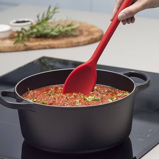 Cuillère en silicone rouge mélange sauce à spaghetti dans casserole