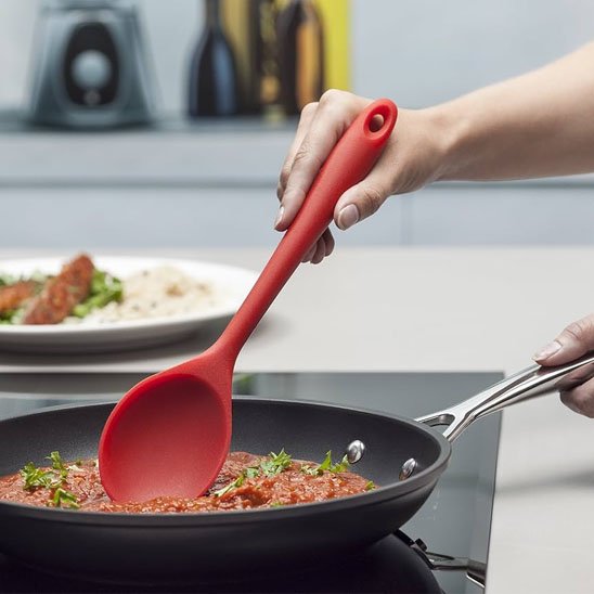 Cuillère en silicone rouge remue sauce à spaghetti dans poêle
