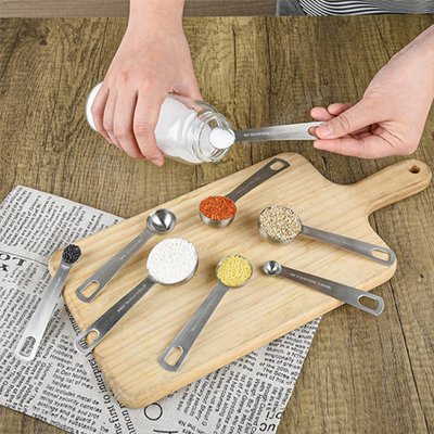 Cuillères doseuses inox contenant ingédients variée sur planche à découper 