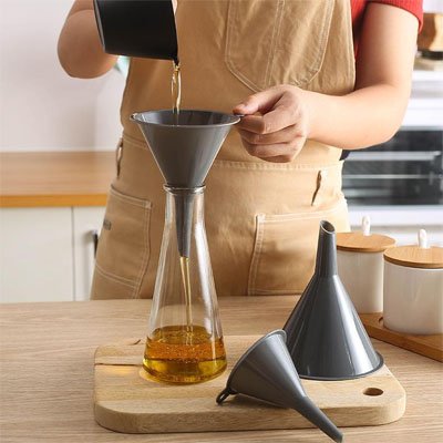 cuisinier utilise entonnoir  pour verser liquide d'une casserole dans bouteille