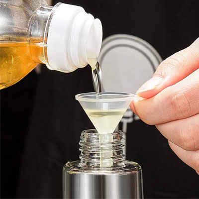 femme  utilise un entonnoir miniature pour verser huile dans bouteille à goulot étroit