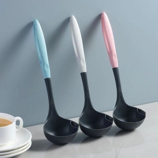 louche en silicone noir avec manche bleu, manche gris et manche rose appuyées contre un mur