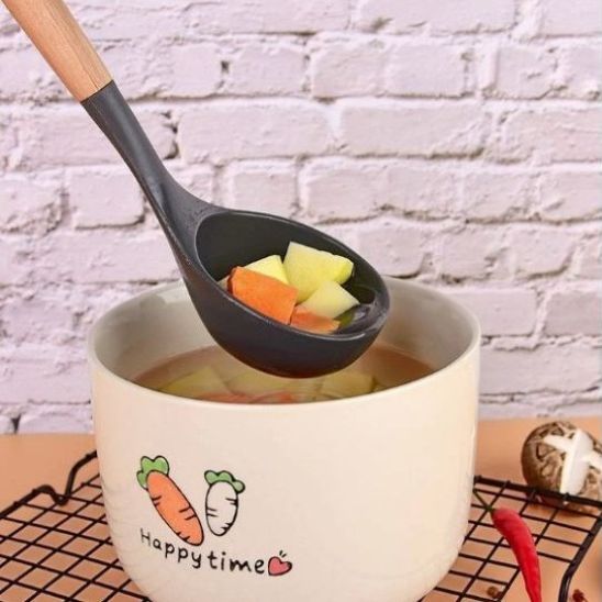 légumes  dans louche en silicone noir tenue au-dessus d'un bol de soupe