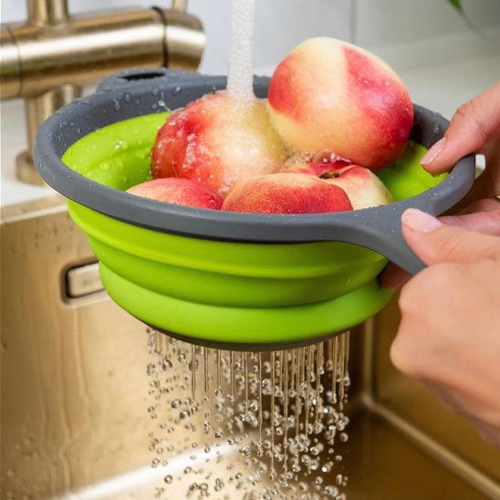 main tenant passoire par poigné rince pommes sous robinet 