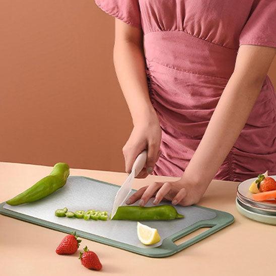 femme-coupe-cocombre-sur coté inox de planche à découper à deux faces