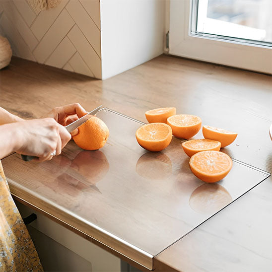 femme-coupe-oranges-sur-planche-à-découper-acrylique-devant-fenêtre