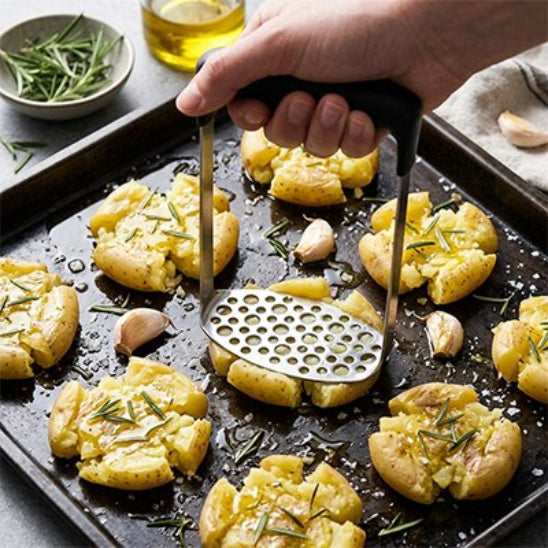 homme écrase pommes de terre sur une plaque de cuisson avec presse purée manuel