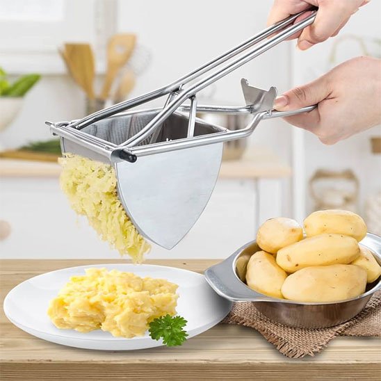 Presse purée écrasant pommes de terre dans assiette blanche auprès de bol de pommes de terre entières