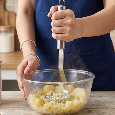 femme écrase pommes de terre dans bol en verre utilisant presse purée