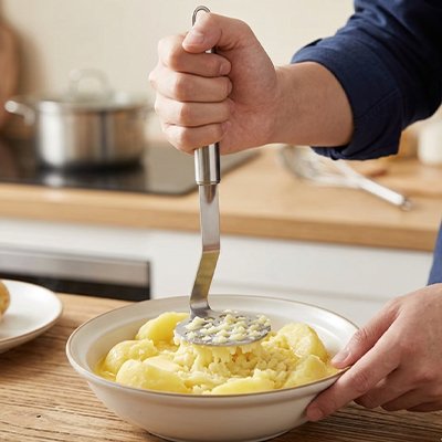 homme écrase pommes de terre dans bol céramqiue utilisant presse purée