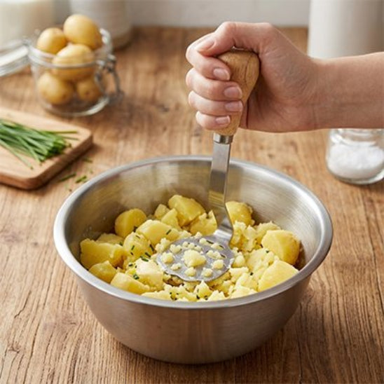 femme écrase pommes de terre dans bol inox avec presse purée miniature