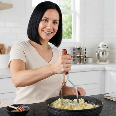 Presse-purée femme écrase pommes de terre dans poêle en fonte