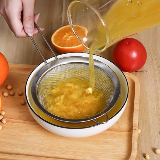 femme filtre jus d'orange avec tamis cuisine inox