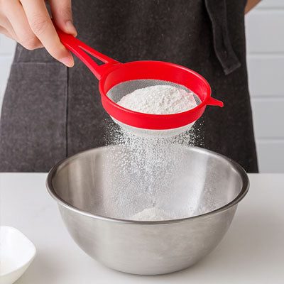 mains féminine tamise farine avec tamis rouge plastique