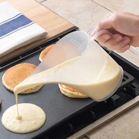 femme verse pâte à pancake sur plaque chaufante d'un verre doseur 