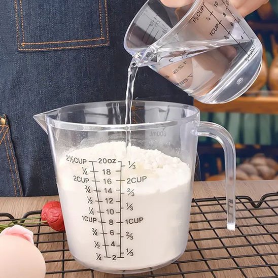 quelqu'un versant eau d'un verre doseur dans un autre contenant farine